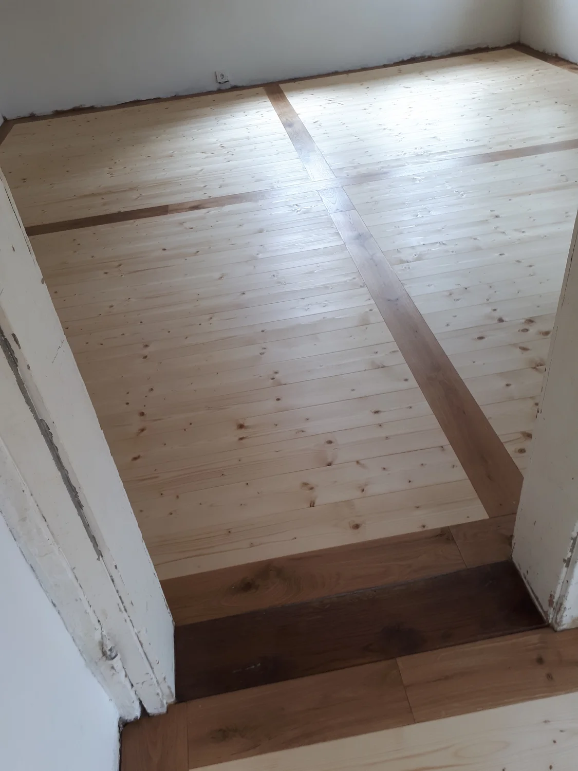 Schreinerei - Maßgefertigte Holzarbeiten - Ein Dielenboden aus Holz, über den diagonal eine breite, dunklere Holzdiele verläuft.