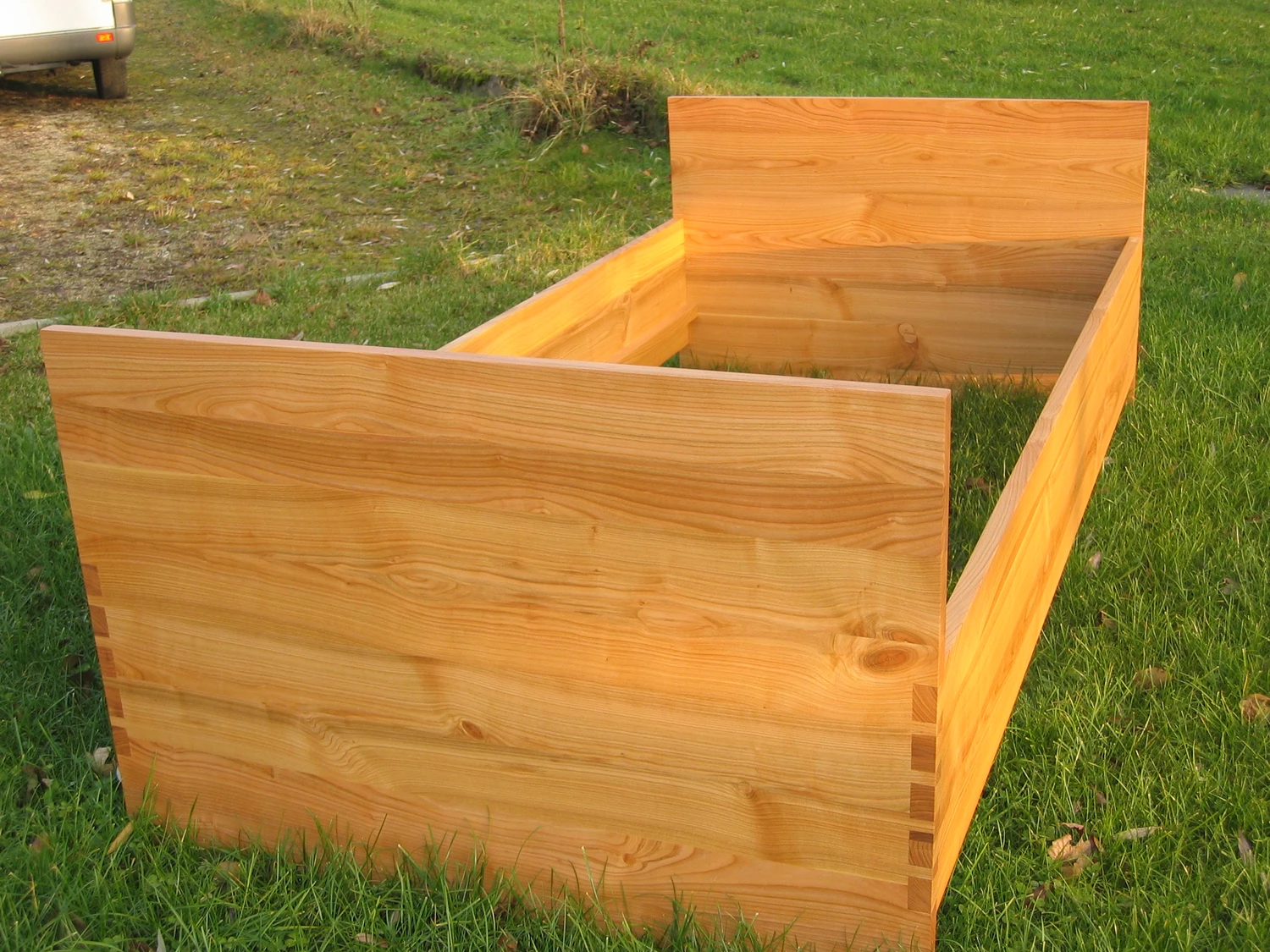 Schreinerei - Maßgefertigte Holzarbeiten - Nahaufnahme von zwei Hochbeeten aus hellen, naturbelassenen Holzbohlen mit sichtbarer Maserung und Eckverbindungen, die auf grünem Rasen stehen.