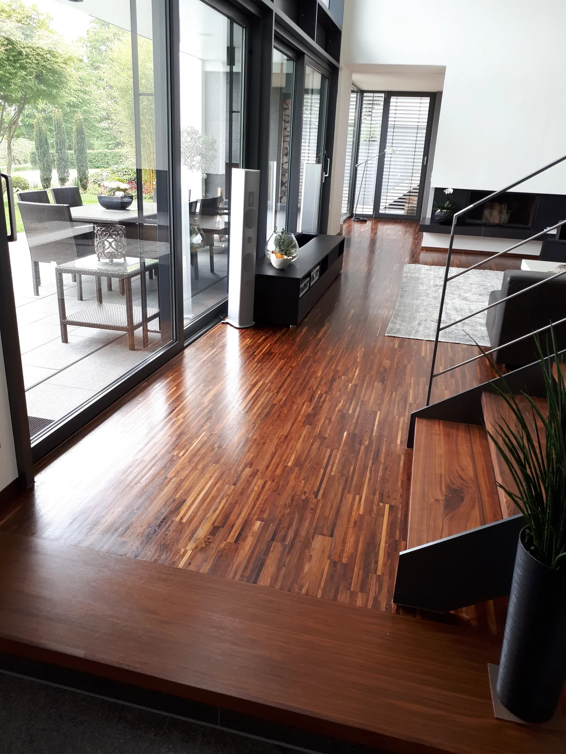 Schreinerei - Maßgefertigte Holzarbeiten - Ein moderner Innenraum mit glänzendem, dunklem Holzparkettboden und einer zeitgenössischen schwarzen Metalltreppe.